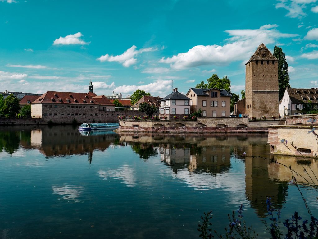 The beautiful Strasbourg on a lovely blue sky day. The picture over the canal with a scenic boat gliding past. The old colourful buildings rise up into the clear sky