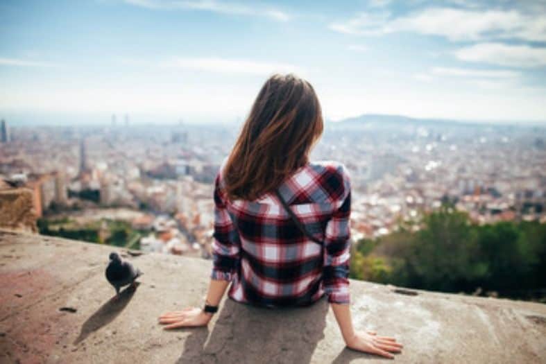 A teenage girl in Barcelona sitting on a ledge in an elevated location above the city