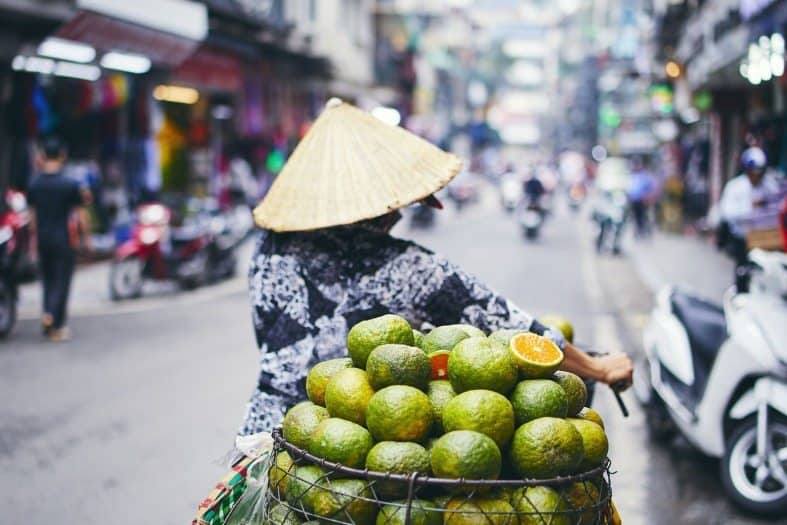 a lady riding a bike in Hanoi with fruit in her basket