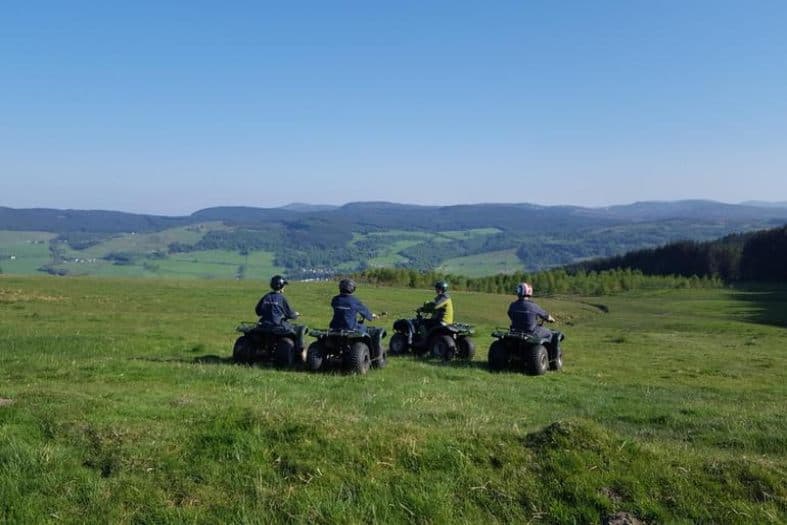 4 teenagers in a lush green field in Scotland on quad bikes on their teens adventure. In the distance, you can see rolling hills at are both green and lush as well as trees.