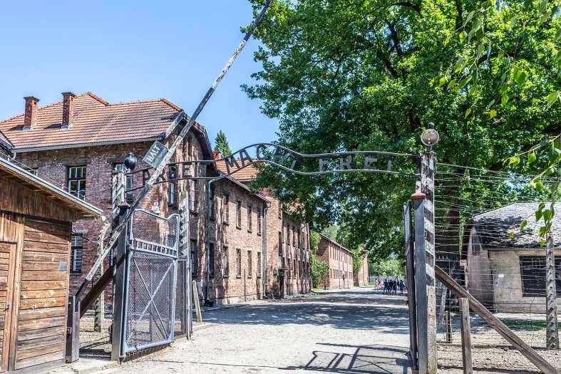 The front gate of Auschwitz Concentration Camp Barracks. The red brick buildings in the background shine bright on a sunny day with the green trees slightly hiding the barbed wire fences. This is one of the first places you will go on your Krakow to Auschwitz tour